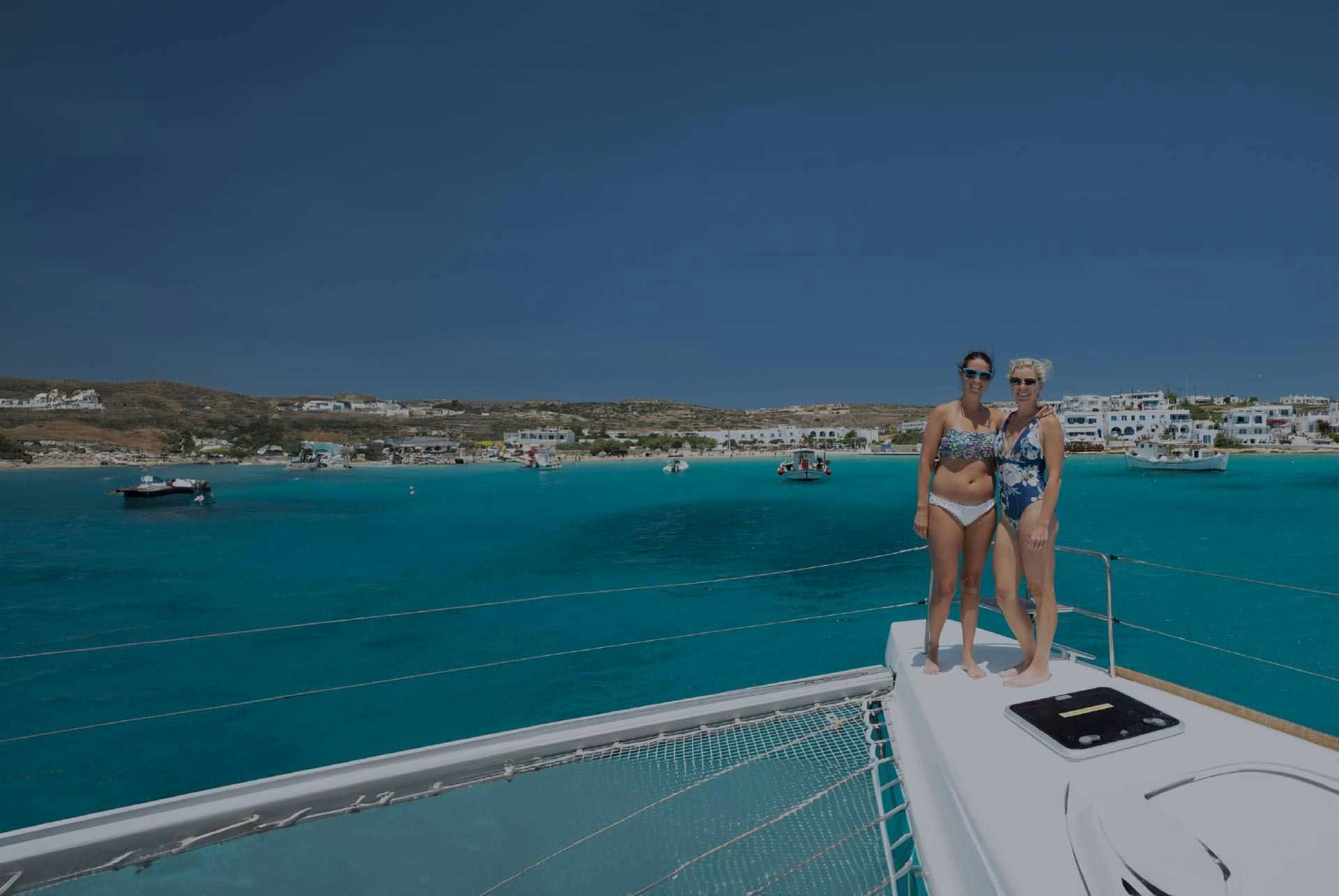 Two women pose for a photo on the bow of a yacht in Greece